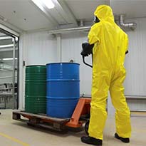 Worker wearing PPE transporting chemicals in barrels