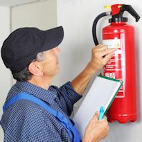 Worker inspecting portable fire extinguisher hanging on wall