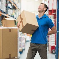 Warehouse worker lifting box and experiencing lower back pain