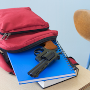 gun coming out of a backpack on a school desk.