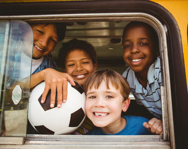 Students on a bus with a ball looking out the window.