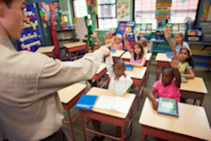 Students in a classroom with their hands raised in the air to answer a question.