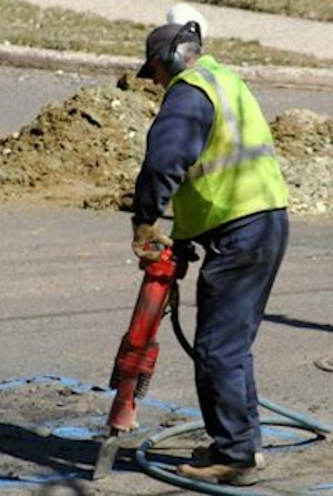 A worker using a jackhammer in the middle of a road.