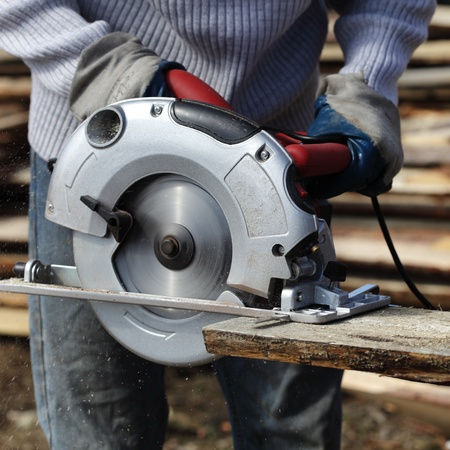 Worker operating a circular saw cutting through a wood board.