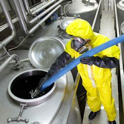 Worker in a HAZMAT suit cleaing out a tank with chemicals.