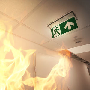 Fire in a hallway underneath an evacuation sign.