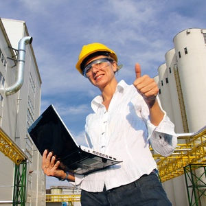 Woman wearing a yellow hard hat, holding a laptop, and giving a thumbs up.