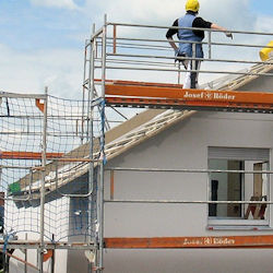 Single worker with helmet standing on scaffolding platform around a house