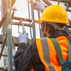 Worker in helmet climbing a ladder outside with fall protection
