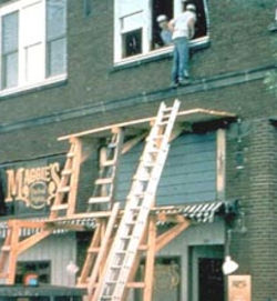 Man climbing through third story window from scaffold that is not tall enough to reach the window>
                        				<span class=