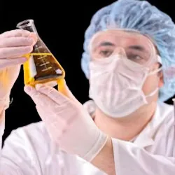 Technician wearing PPE and holding a beaker of yellow liquid