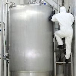 Worker in PPE climbing ladder next to stationary container