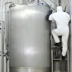 Worker in PPE climbing ladder next to stationary container