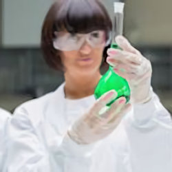 Lab worker in PPE holding beaker with green liquid