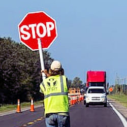 A human flagger wearing the proper safety equipment and holding a STOP sign to stop oncoming traffic.