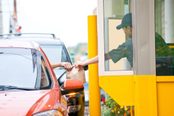 Worker handing food to a customer at a drive thru window.