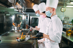 Cooks cooking food on stoves in a restaurant kitchen.