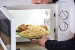 Person placing plate of food in a microwave.