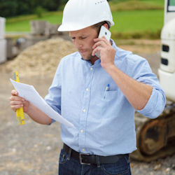Employer is outside looking at paperwork and speaking on smart phone.