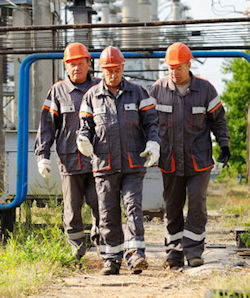 Three employees walking on a dirt path through a refinery.