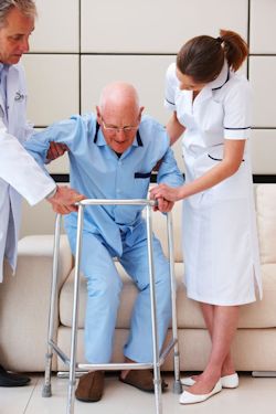 Doctor and nurse assisting an elderly man to get up from a couch.