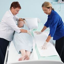 Two healthcare providers shifting a patient in bed.