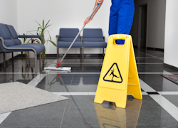 employee mopping floor with slipping hazard sign displayed.