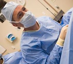 Healthcare provider wearing a gown, gloves, and mask in a surgical room.