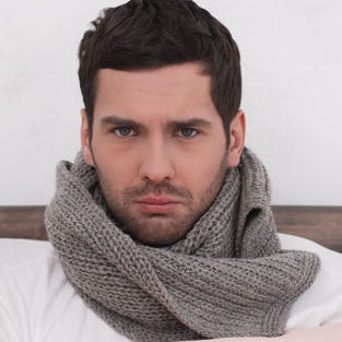 A man sits in bed wearing a
                                        gray scarf wrapped around his neck.
