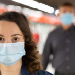 Woman wearing a face mask. There is a man in the background wearing a face mask.