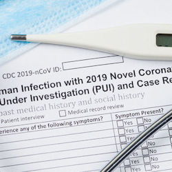 part of a stethoscope and thermometer on top of a COVID-19 case report form