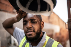 Worker in a yellow safety vest wipes sweat from his forehead.