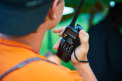 Back of man's head and shoulder who is wearing an orange shirt and holding a communication radio