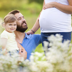 a husband, pregnant wife, and daughter in a field of flowers.