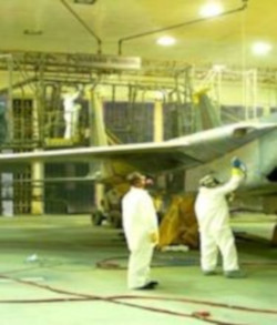 Two painters in PPE using a paint sprayer to paint a plane.