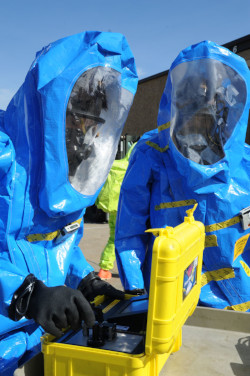 Two workers in fully encapsulating suits picking items out of a small case