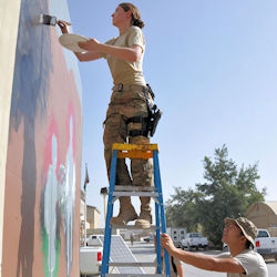 worker is unsafe standing on a ladder using both hands to paint a wall