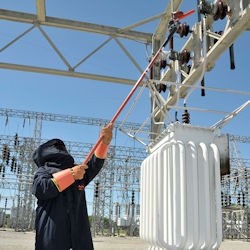 Worker using tool to reach up to overhead power line