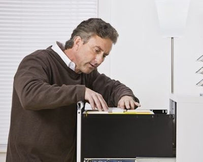 Worker at top drawer of file cabinet searching for records