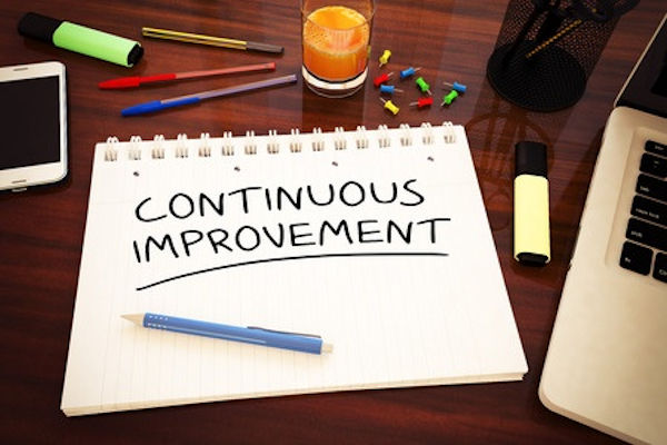 The words Continuous Improvement written on a notebook page sitting on a desktop