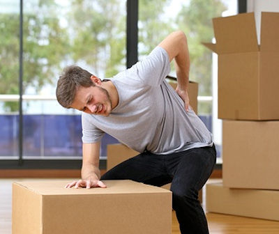 Man in pain with hand on back leaning over a box