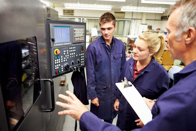Two workers overseeing instructor giving on the job training in front of a operator panel