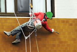 Worker overreaching and dangling from fall protection to reach area of a outside wall