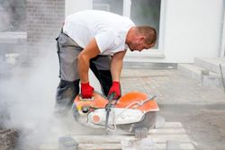 Worker hunched over cutting cement without proper PPE