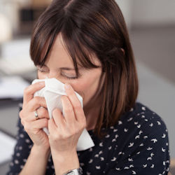 Person using tissue to wipe nose and cover mouth