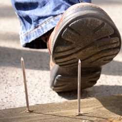 worker wearing safety shoes about to step on a long sharp protruding nail wearing safety shoes