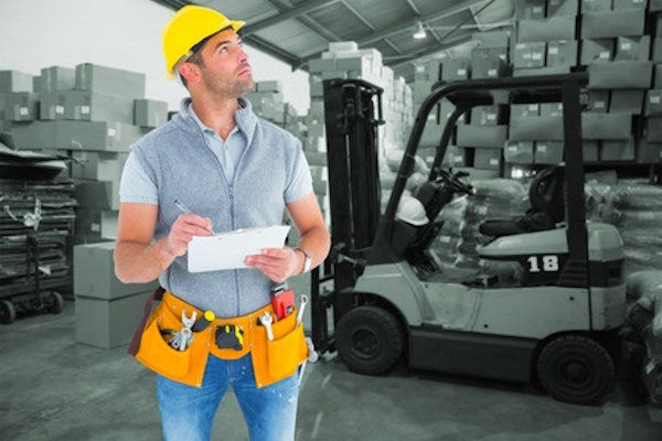 Single worker walking around worksite doing an inspection and taking notes.