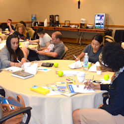 Employees at orientation sitting at round tables taking notes.