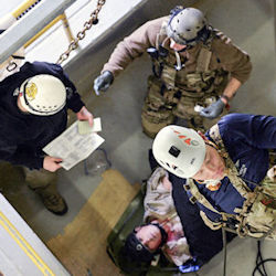 Three rescuers around a man laying on the ground who has been rescued