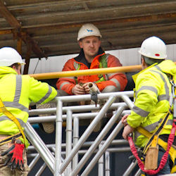 three workers on a scaffold discussing scaffold hazards